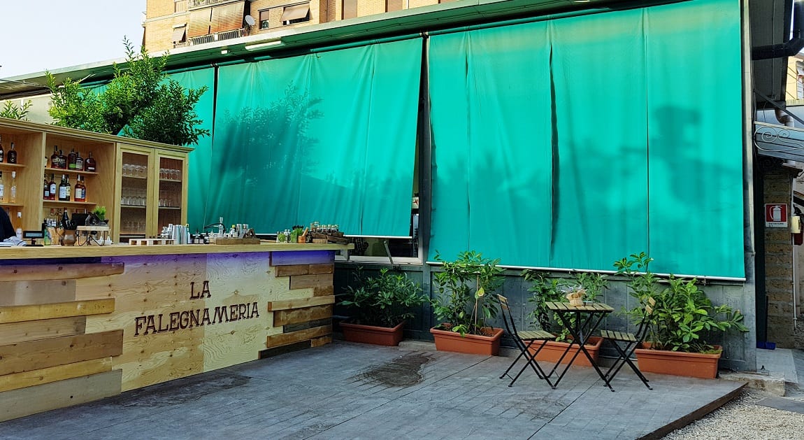 Il cortile della falegnameria trasformato in cocktail bar con bancone in legno, sedie e tavoli da esterno