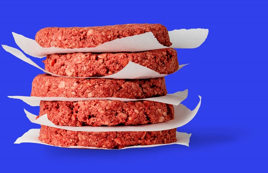 Cinque hamburger di fake meat impilati, pronti da cuocere, su fondo blu