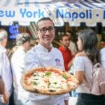 Gino Sorbillo presenta una pizza Margherita davanti a una delle sue pizzerie