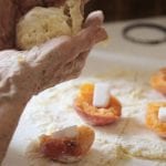 Mani di una nonna in cucina con l'impasto per un dolce alle albicocche
