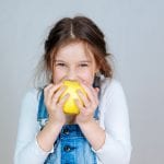 Una bimba di 7 anni addenta una mela gialla e sorride