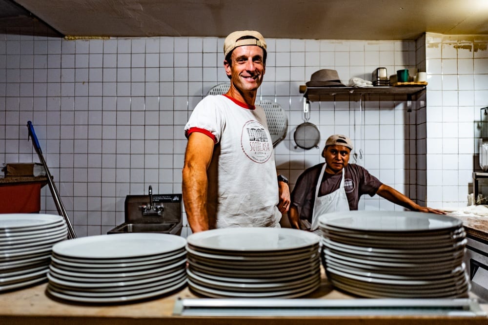 Luca Arrigoni nella sua pizzeria, con i piatti da pizza impilati
