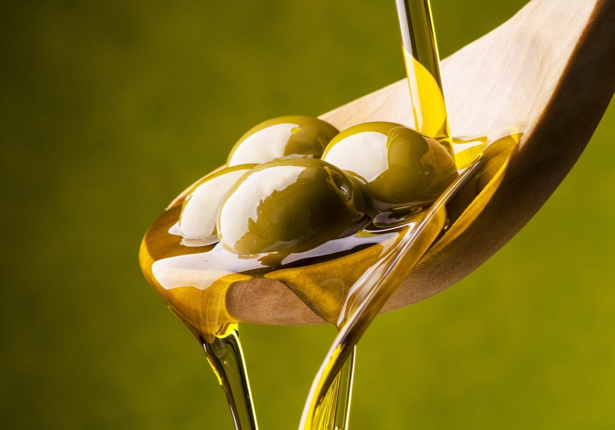 olio di oliva versato su un cucchiaio in legno con olive