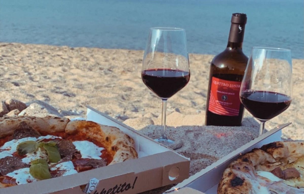 Pizze da asporto mangiate in spiaggia, con vino rosso