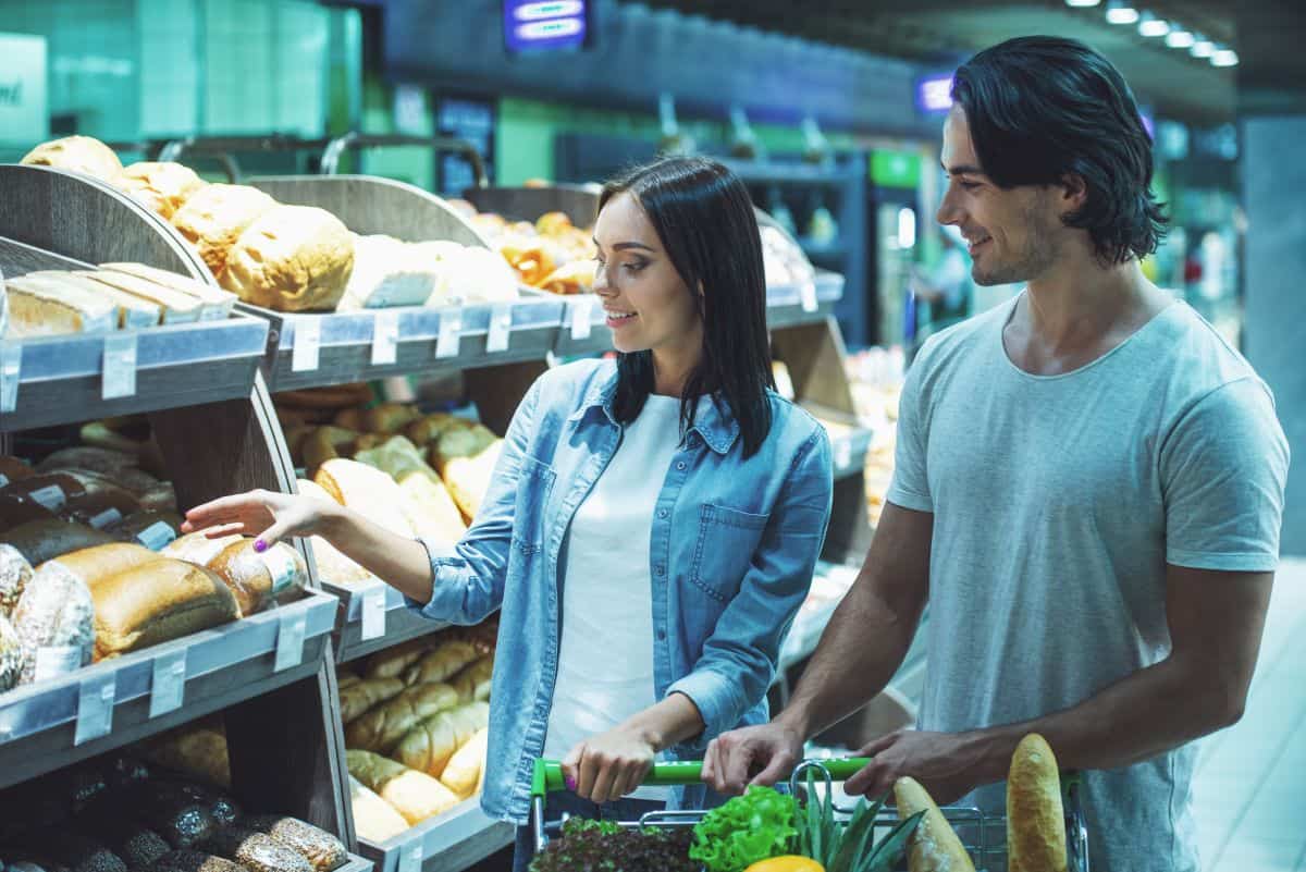 Beautiful young couple leaning on a shopping cart, smiling while choosing food in a supermarket