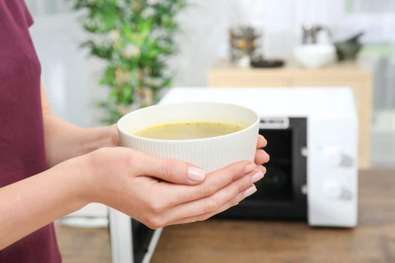 Woman holding bowl with tasty soup in kitchen