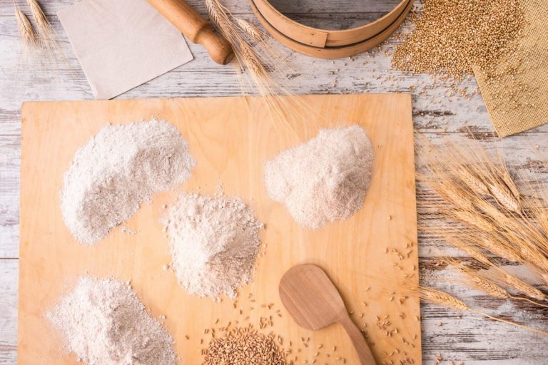 Farine integrali diverse sull’asse di legno con chicchi e spighe