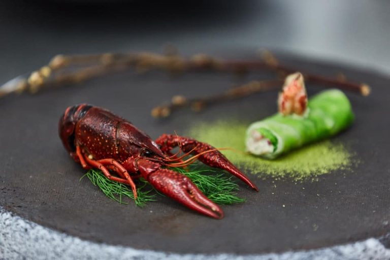 Gamberi della Louisiana su piatto d'ardesia con involtino vegetale ripieno||Un gambero della Louisiana mostrato dalla mano di una commensale che gusta i piatti di Holycrab