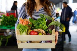 Una cassetta di frutta e verdura tra le mani di una ragazza con maglia a righe||
