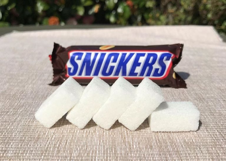 Una barretta di Snickers e le zollette di zucchero in primo piano|