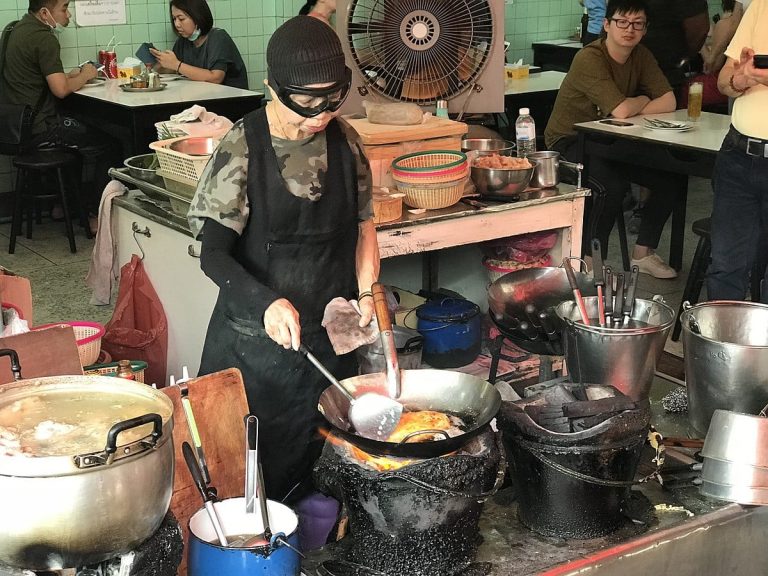 Jay Fai al lavoro con la maschera davanti alla padella delle omelette