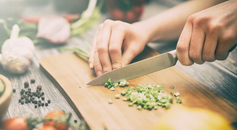 Mani che tagliano verdure su un tagliere