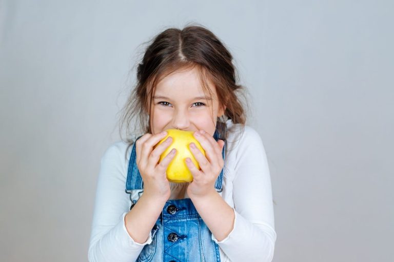 Una bimba di 7 anni addenta una mela gialla e sorride|Una mamma prepara la merenda per la scuola