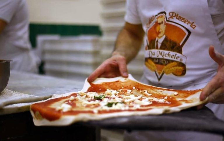 Un pizzaiolo condisce la pizza Margherita prima di infornarla