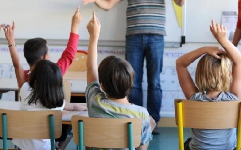 Tre bambini seduti di spalle in classe alzano la mano