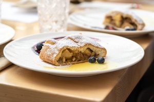 Una fetta di strudel di mele con crema e mirtilli||gara di strudel: una giurata valuta una fetta di strudel e prende appunti