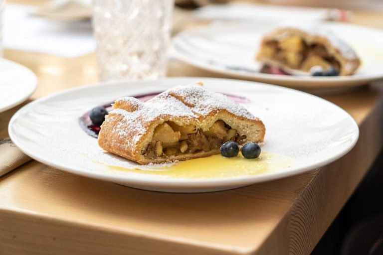 Una fetta di strudel di mele con crema e mirtilli||gara di strudel: una giurata valuta una fetta di strudel e prende appunti