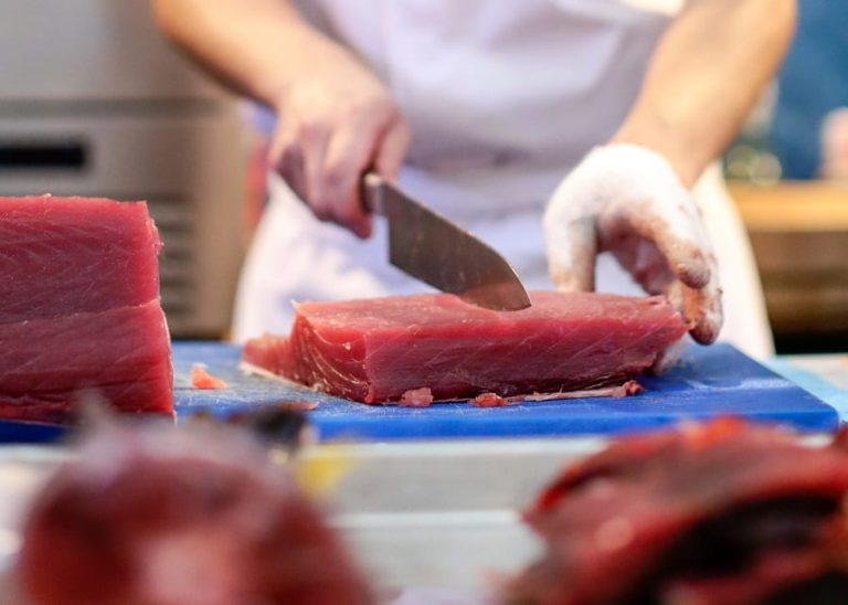 Uno chef taglia tonno fresco in cucina|Un tonno fresco intero su tagliere di legno