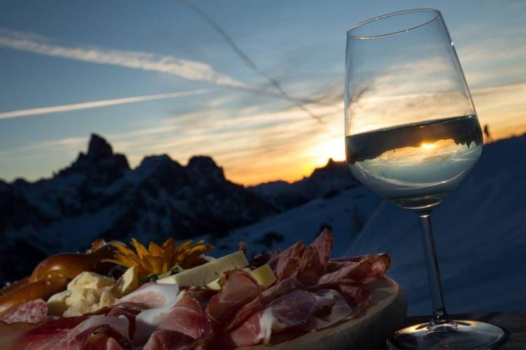 Tagliere di salumi e calice di bollicine al tramonto sulle Dolomiti innevate