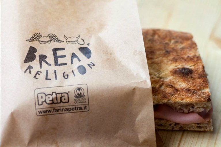 Pezzo di pizza bianca con salume avvolto in carta intestata bread religion|Persona versa il vino bianco al Collisioni Festival|Collisioni Festival 2019. Foto di Alessia Conte|Collisioni Festival 2019. Hamburger di Eugenio Roncoroni