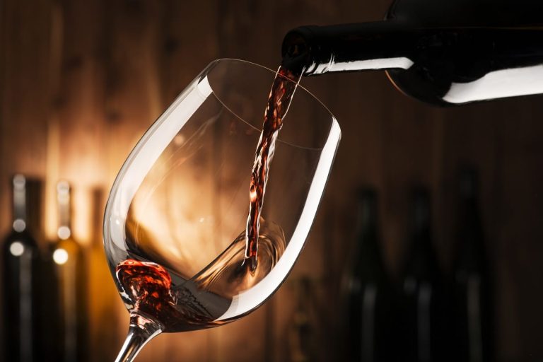 Un calice di vino rosso versato dalla bottiglia