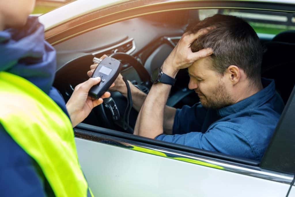 drink and drive concept - sad drunk man sitting in the car after police alcohol test with alcometer