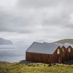 Strutture per l’essiccazione del pesce e paesaggio oceanico nelle Isole Faroe con villaggi vichinghi e cielo nuvoloso
