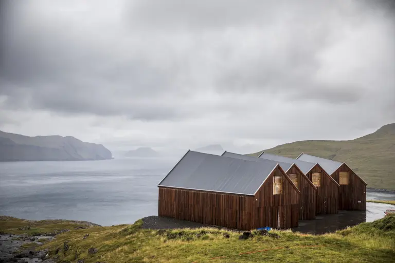 Strutture per l’essiccazione del pesce e paesaggio oceanico nelle Isole Faroe con villaggi vichinghi e cielo nuvoloso