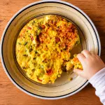 Mano di un bambino che prende una fetta di frittata fatta in casa