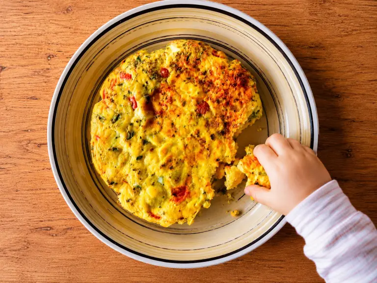Mano di un bambino che prende una fetta di frittata fatta in casa
