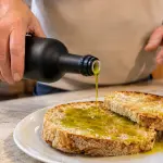 Olio extravergine umbro versato in una ciotola tra olive fresche