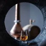 Bicchiere di distillato ambrato accanto a una botte di Mizunara, rara quercia giapponese usata per whisky e grappa