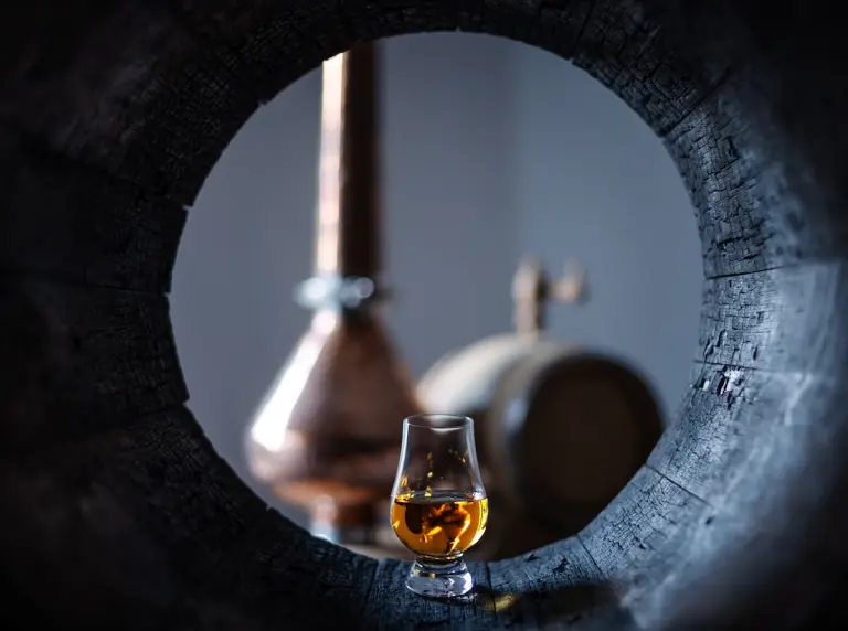 Bicchiere di distillato ambrato accanto a una botte di Mizunara, rara quercia giapponese usata per whisky e grappa