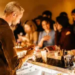 Bancone di cocktail bar affollato ai Navigli di Milano con bartender al lavoro e drink colorati serviti ai clienti