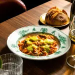 Piatto gourmet servito da Élevage Restaurant con calice di vino bianco sul tavolo