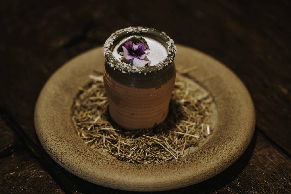 Un cocktail di Apelle, servito in tazza di ceramica su piatto con fieno