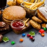 Cibo da fast food: un panino con hamburger, salsa ketchup, patatine fritte, caramelle gommose, cioccolato, cookies, muffin ai mirtilli, coca cola