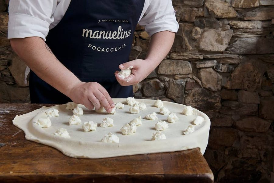 La preparazione della focaccia di Recco, con i fiocchi di stracchino disposti sulla sfoglia di pasta da un cuoco di Manuelina