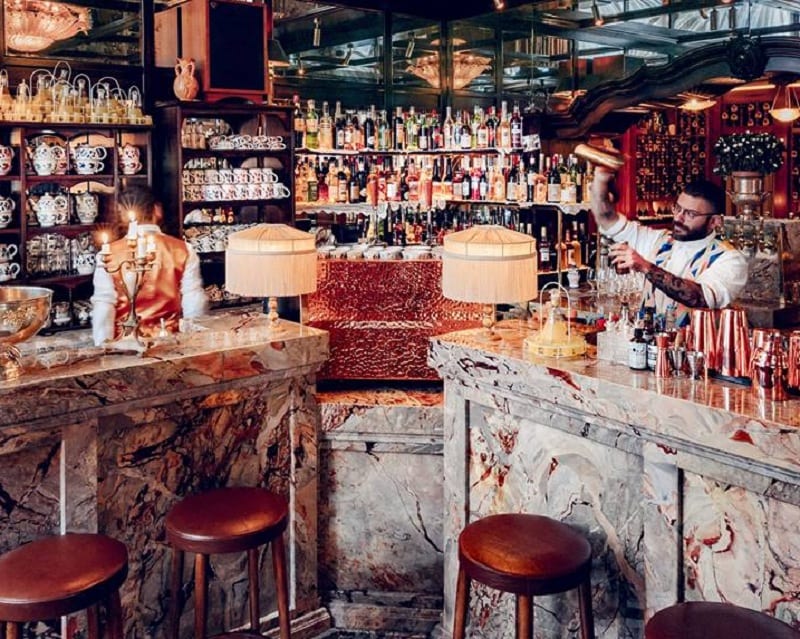 Il bar con bnachi in marmo di Carrara, sgabelli imbottiti, bottigliera a parete e soffitto specchiato, con du barman intenti a miscelare