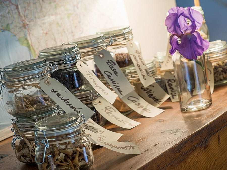 Le erbe aromatiche dentro barattoli in vetro con etichette scritte a meno, su una mensola in legno e un fiore d'iris viola