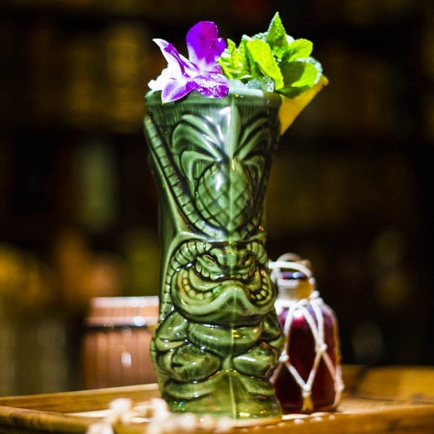 Un tiki cocktail in tiki mug verde decorata con fiori viola e menta