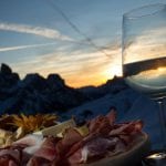 Tagliere di salumi e calice di bollicine al tramonto sulle Dolomiti innevate