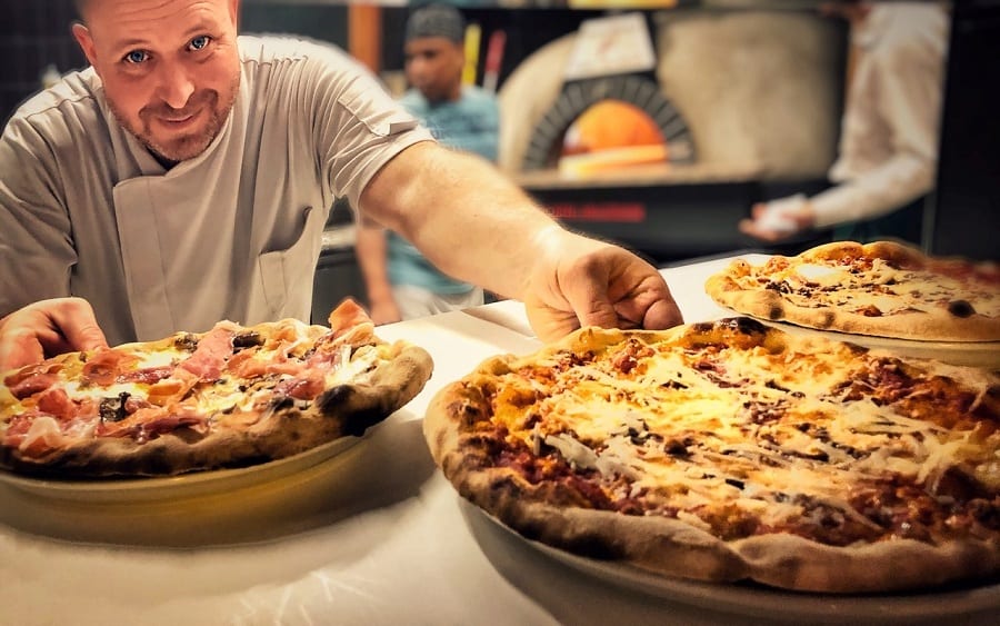 Alessandro Angelieri serve due pizze al TreeToo. Sullo sfondo il forno a legna
