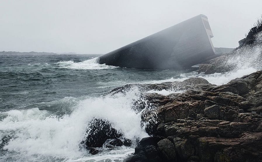 Il monolite di Under che emerge dalle onde sulla scogliere norvegese di Baly