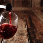 Vino rosso versato nel bicchiere da una bottiglia, sfondo in legno