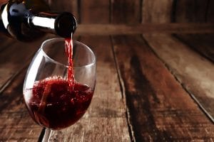 Vino rosso versato nel bicchiere da una bottiglia, sfondo in legno