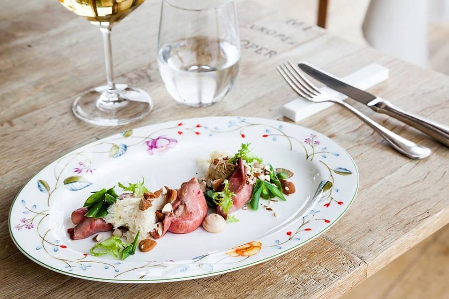 I ravioli di girello del ristorante Vite, nella mise en place con piatto decorato a fiori, tavolo di legno nudo, calice di vino bianco